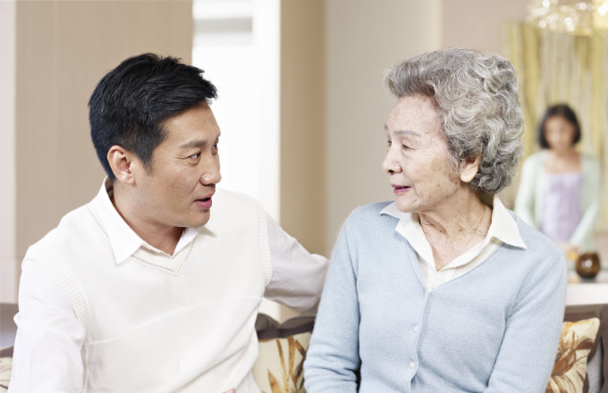 asian mother and adult son chatting on couch